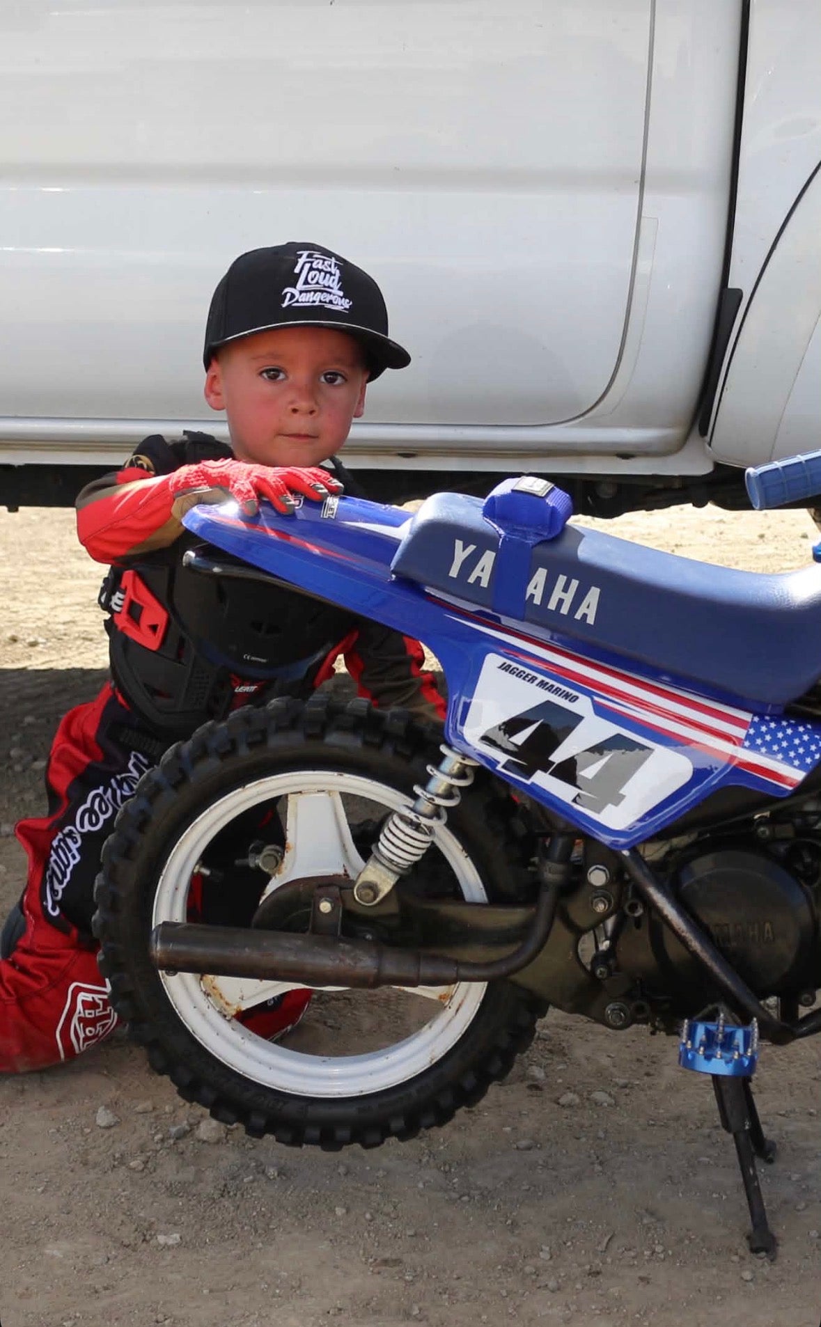 FLD grom wearing FLD Grom hat next to his motorcycle.